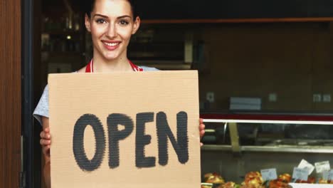 Female-baker-holding-open-signboard