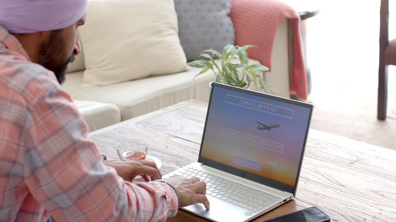 Booking travel online, man using laptop at home with smartphone nearby