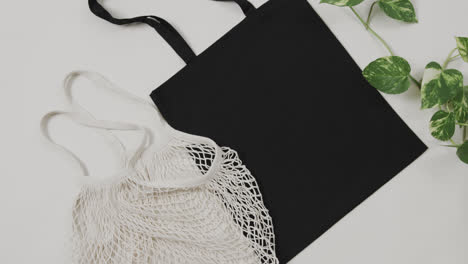 close up of white and black bags with green plant on white background, with copy space, slow motion