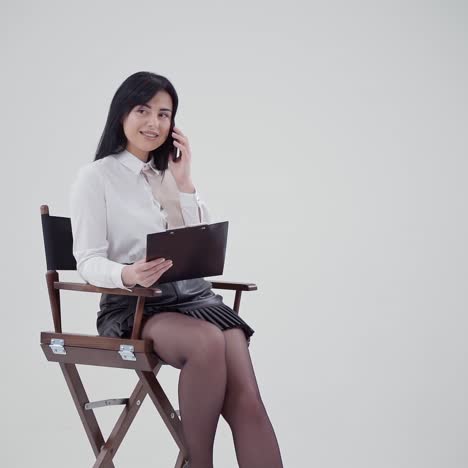 brunette girl talking the phone isolated in studio. young business woman in white blouse sitting in the chair with a folder and speaking the mobile phone. slow motion.