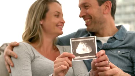 happy future parents on sofa showing sonogram