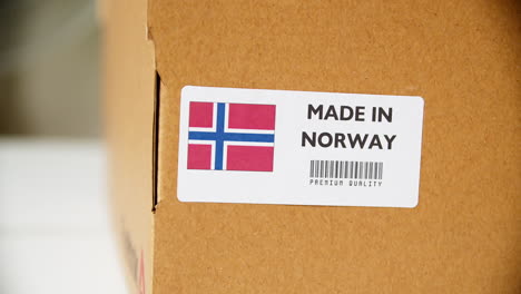 hands applying made in norway flag label on a shipping cardboard box with products