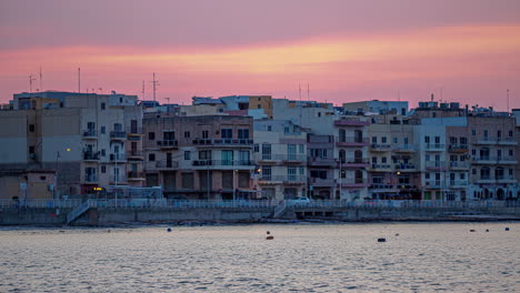 shot of waterfront city buildings of gzira, il-gzira, malta as sunset sky fade at dusk in timelapse