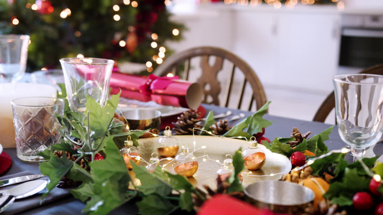 A dining table prepared for Christmas dinner, with a Christmas tree and kitchen background, camera pans along the table