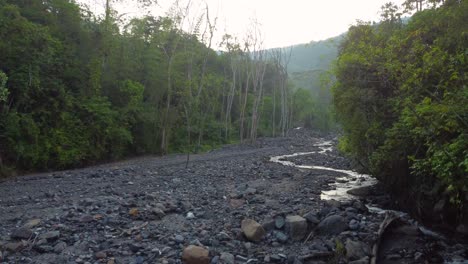 Eine-Niedrige-Drohnenaufnahme,-Die-Einen-Felsigen,-Trockenen-Fluss-Verfolgt,-Der-Bei-Sonnenaufgang-In-Risaralda,-Kolumbien,-Von-Waldbäumen-Umgeben-Ist