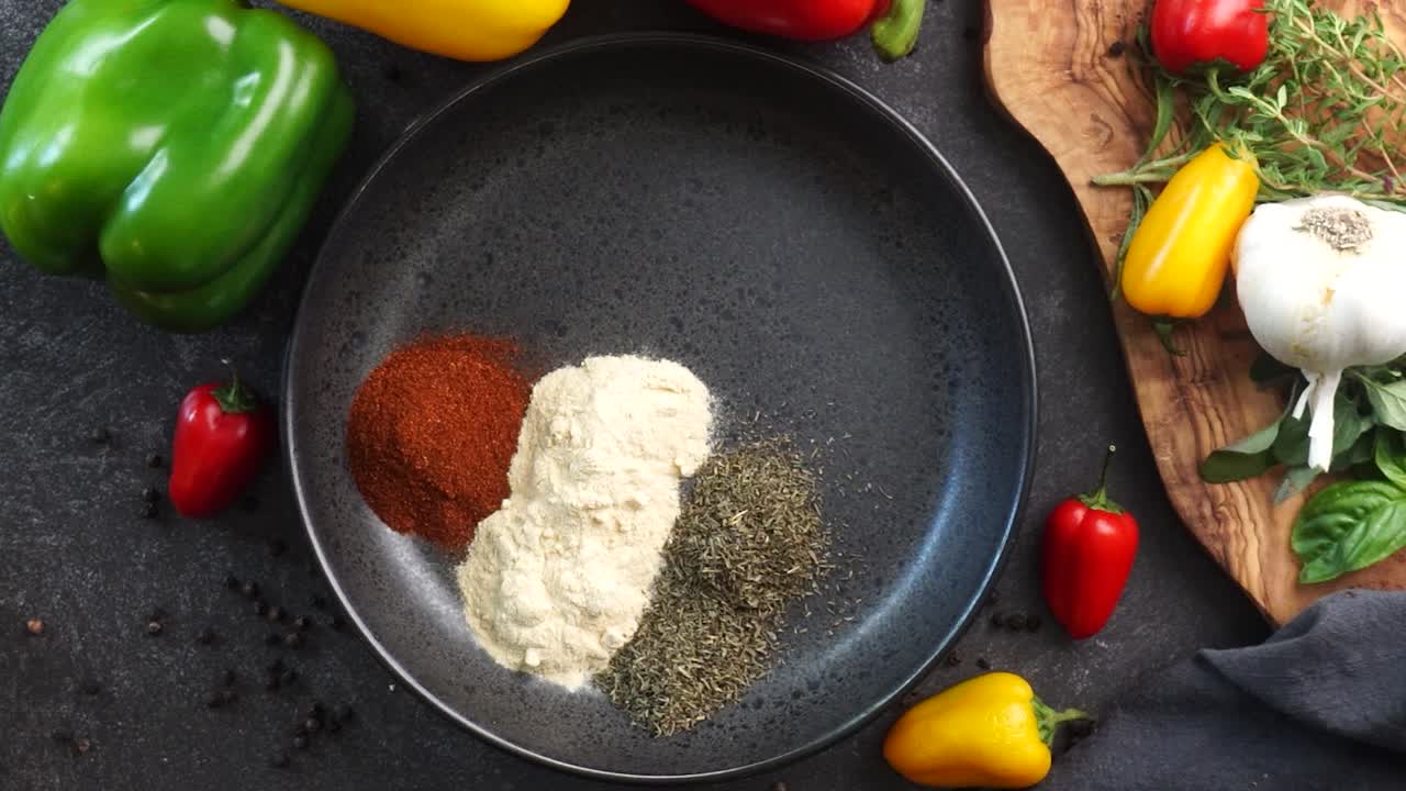 Making a vibrant Cajun Spice Blend, mixing red paprika, cayenne pepper, oregano, thyme, white garlic onion powder and black pepper in a bowl, creating a striking contrast against a black background.