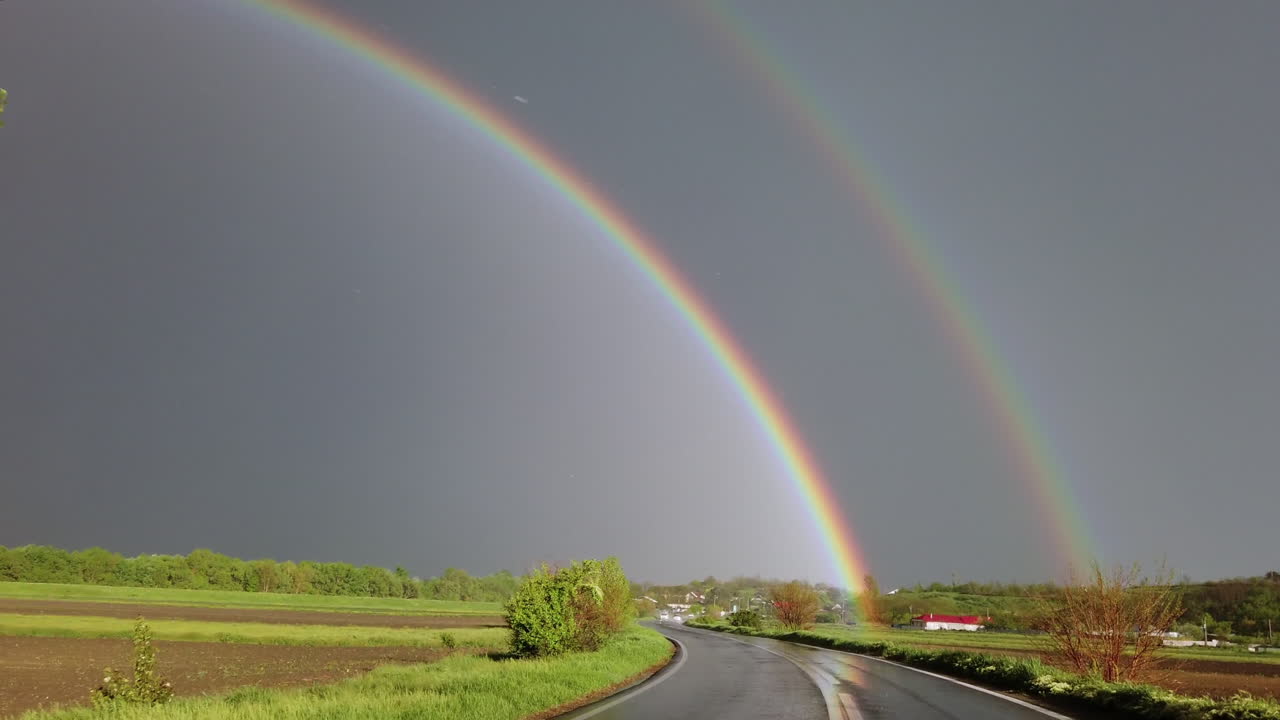 Rainy road with a double rainbow on the horizon
