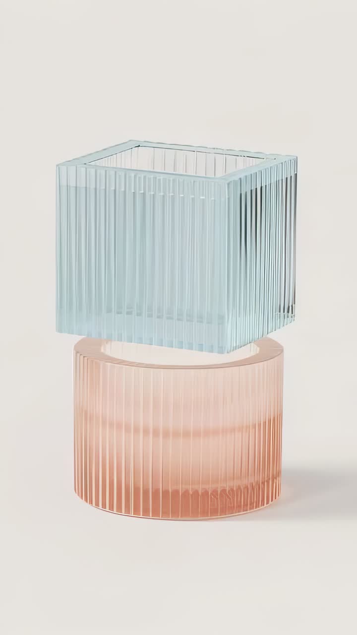 Vertical video: Lifting blue cube rotating above peach cylinder on pale surface under soft light
