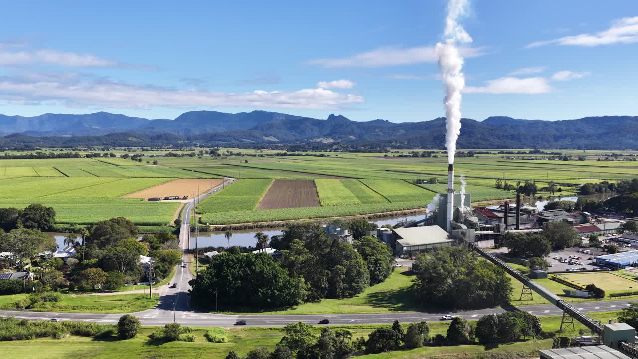 Aerial footage of a sugar mill surrounded by lush fields under clear skies in Murwillumbah, NSW