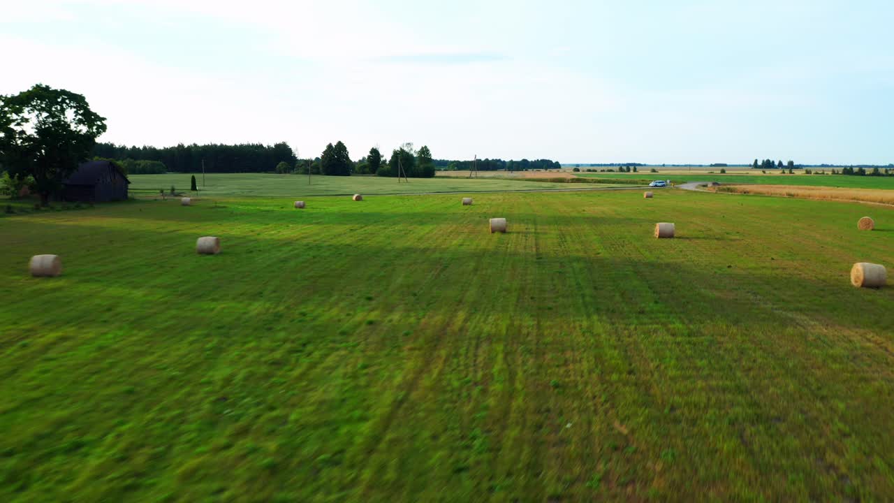 Rapido sorvolo di un paesaggio verdeggiante con balle di fieno sparse nella campagna.