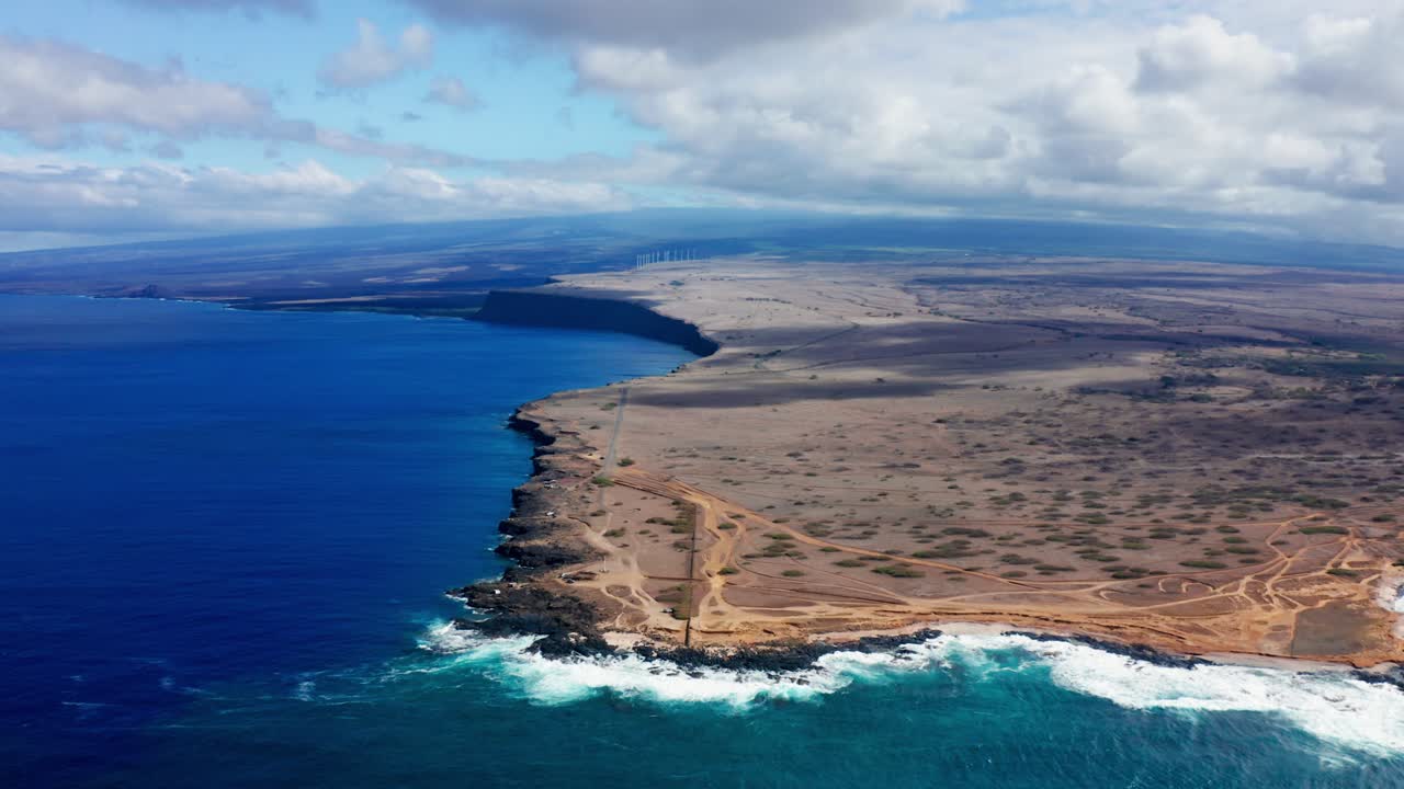Curving trails lead to the ocean’s edge where rust-colored lava fields descend into a foaming shoreline, capturing the stark contrast of earth and sea under textured clouds