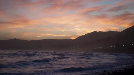 sunset over the ocean with mountains in the background