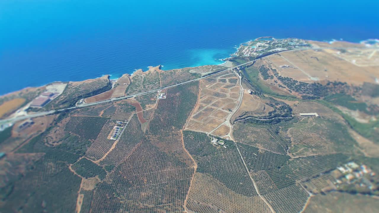 the drone is flying towards sandy beaches and azure waters of Crete. Hovering at 500 meters, . Below, the main road from Heraklion to Rethymno, capturing the essence of a Greek summer