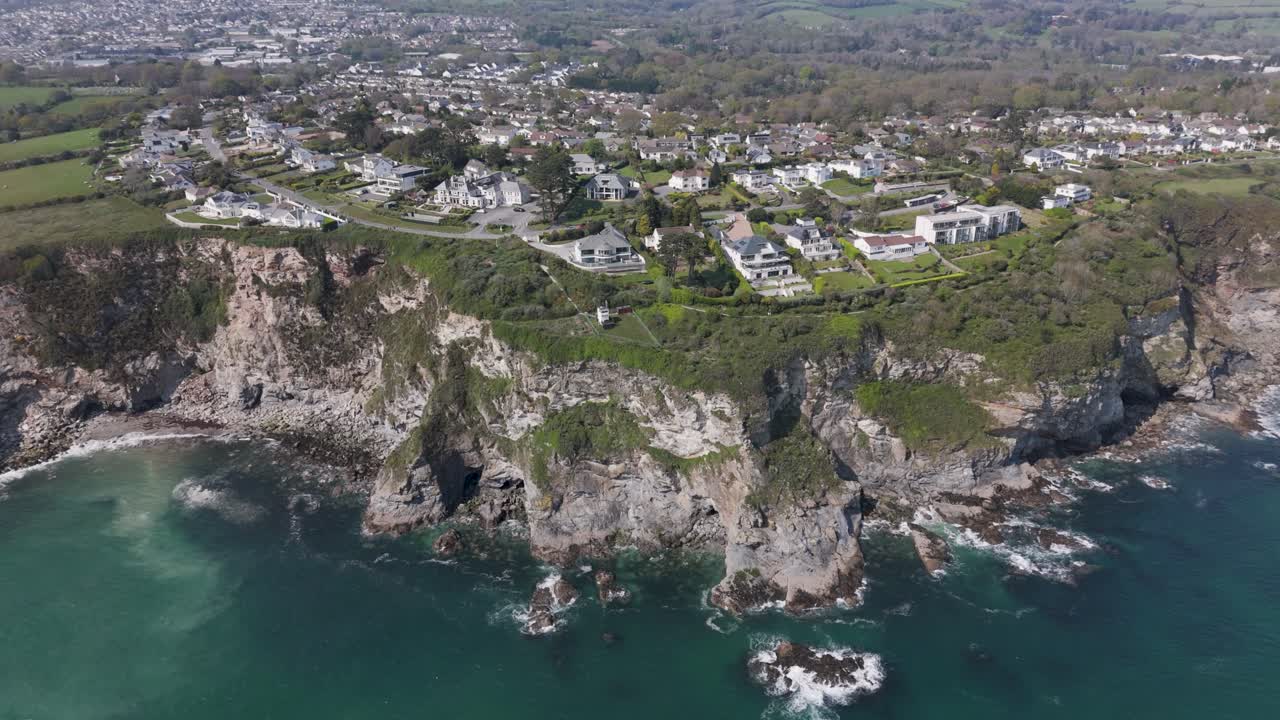 Aerial view of modern cliff-edge villas with panoramic glass, private terraces and landscaped gardens overlooking turquoise waves and rugged shoreline