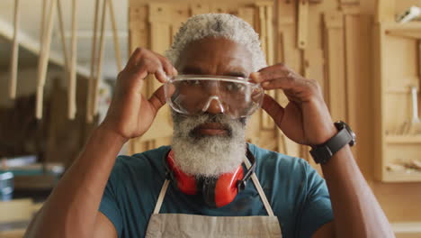 portrait of african american male carpenter wearing safety glasses in a carpentry shop