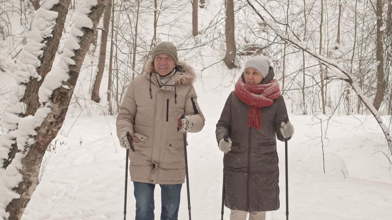 una pareja mayor con raquetas de nieve en un bosque nevado.