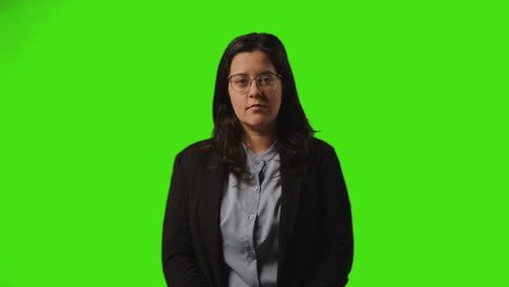 studio portrait of smiling businesswoman wearing glasses folding arms standing against green screen background
