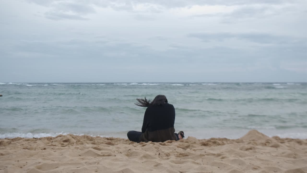 The Back of a Woman With Mental Illness Seeks Solace at the Beach - Static Shot