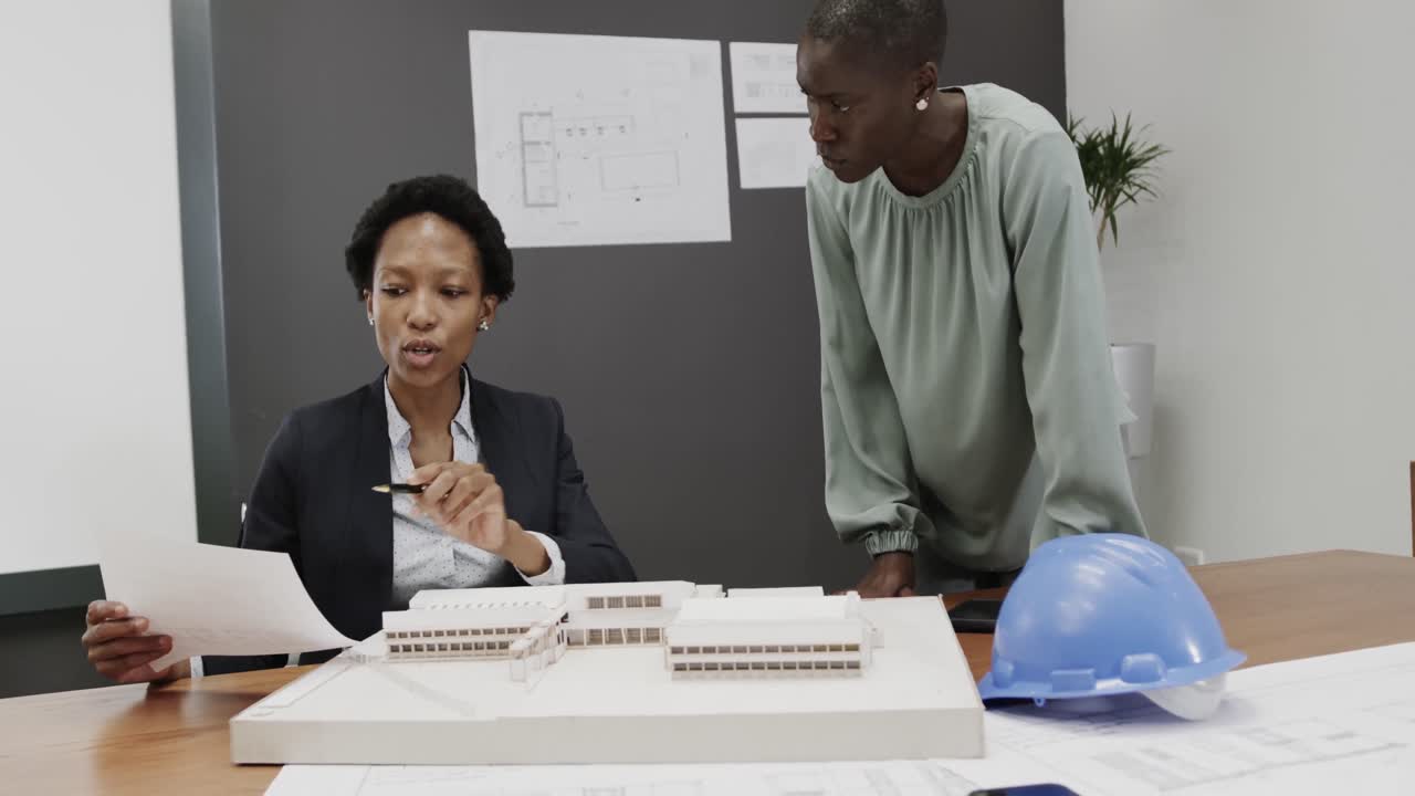 African american female architects discussing blueprints in office, in slow motion