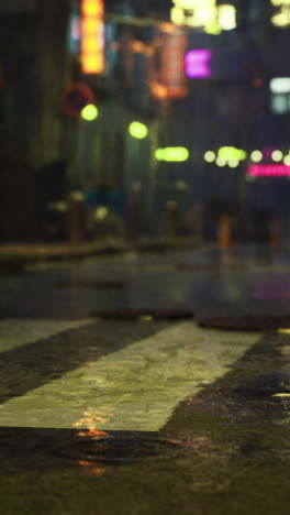 Nighttime urban street reflects neon lights and rain in a busy city