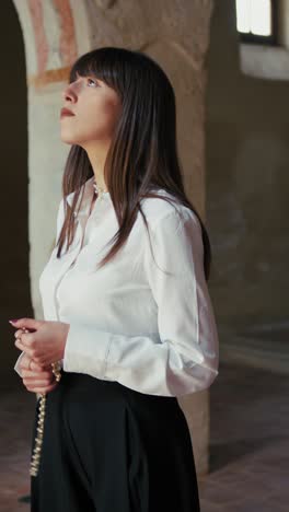 woman praying in devotion with a rosary in the hands inside a church