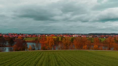 beautiful panorama which includes blue cloudy sky country houses with red roofs lake with autumn trees and green field beautiful colors