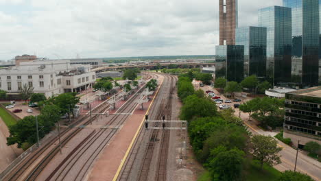 Forwards-fly-above-empty-railway-tracks-in-station.-Group-of-tall-modern-building-with-glass-facade-on-side.-Dallas,-Texas,-US