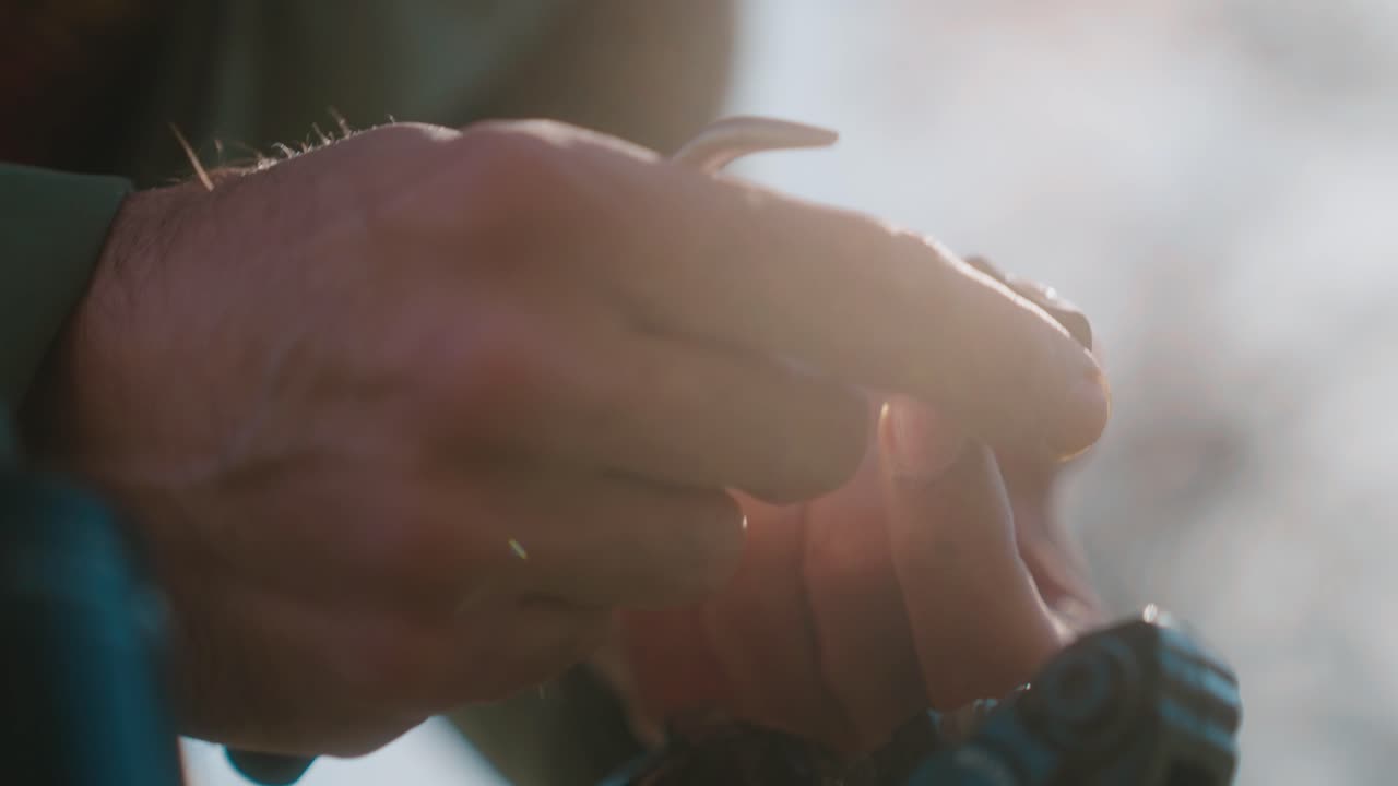 A close-up of hands adjusting a small tool outdoors with soft sunlight shining in the background