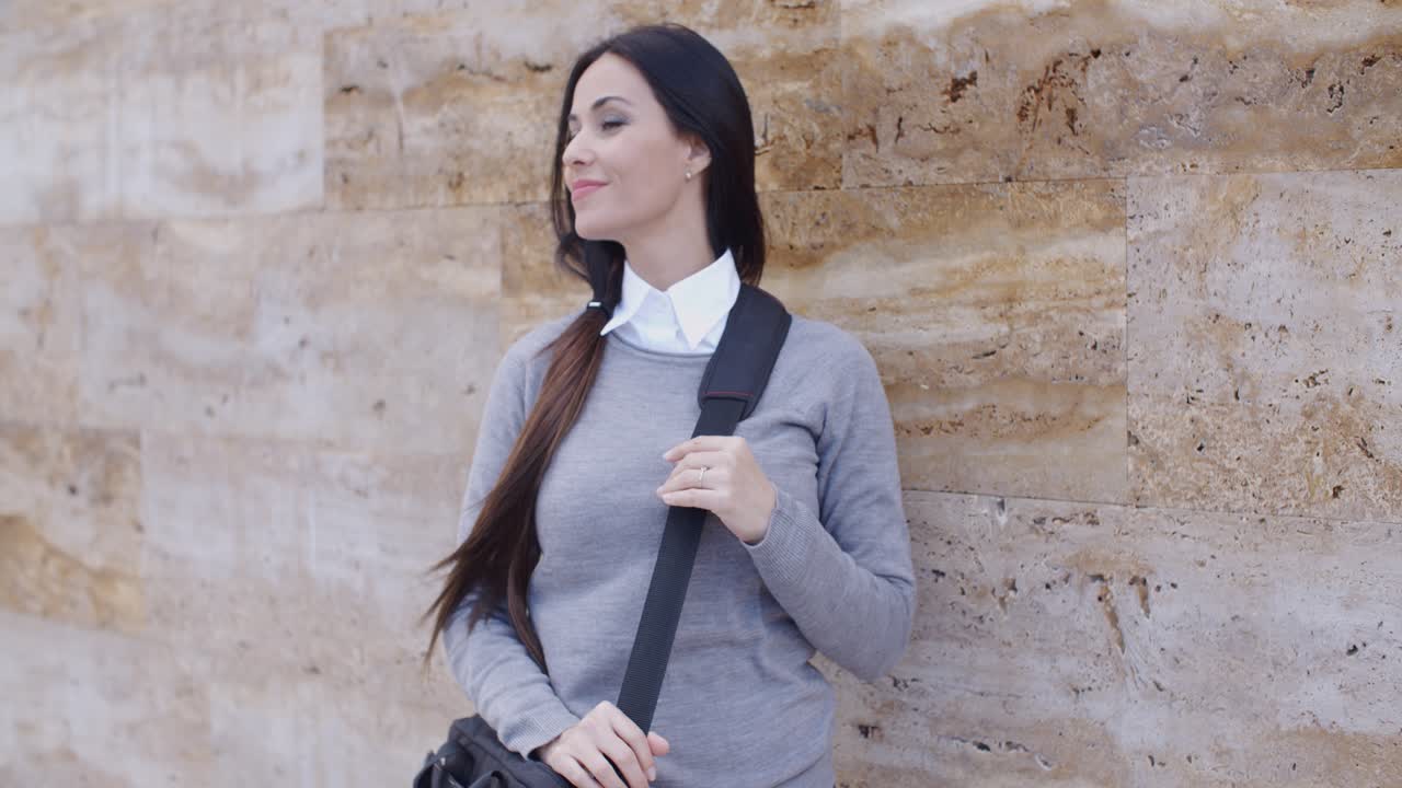 Donna sorridente con un maglione vicino a un muro che guarda oltre