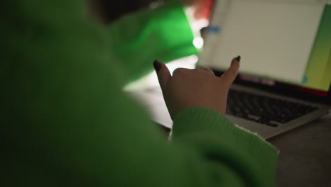 mujer con un suéter verde trabajando en una computadora portátil mientras sostiene un teléfono inteligente. capturada con una cámara de mano, la escena destaca la multitarea, la productividad y el espacio de trabajo digital moderno