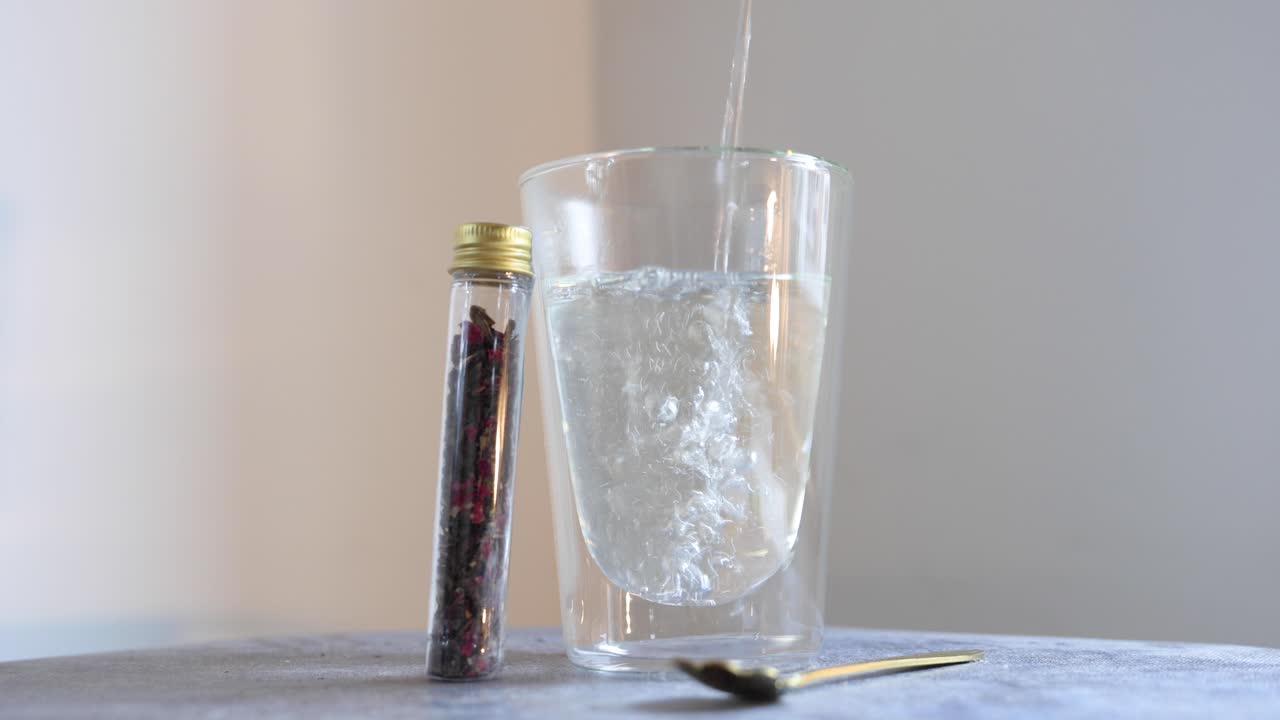 Versare acqua calda in un bicchiere a doppia parete accanto a erbe da tè.