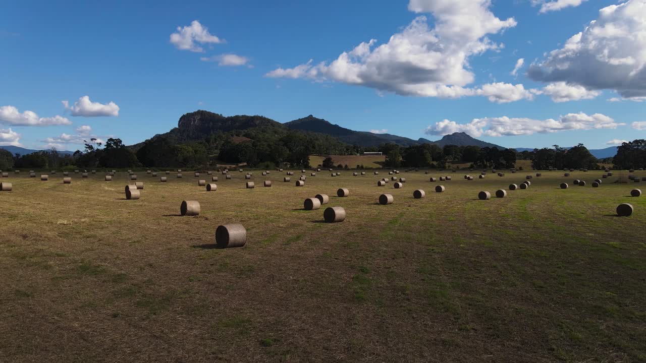 un video de un dron en movimiento lento volando sobre fardos de heno recién enrollados con una cadena montañosa en primer plano