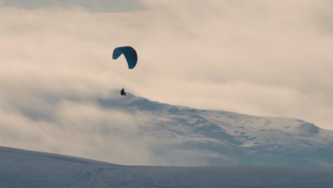 parapente disparó contra la luz con colinas cubiertas de nieve y nubes en el fondo, cumbria, reino unido