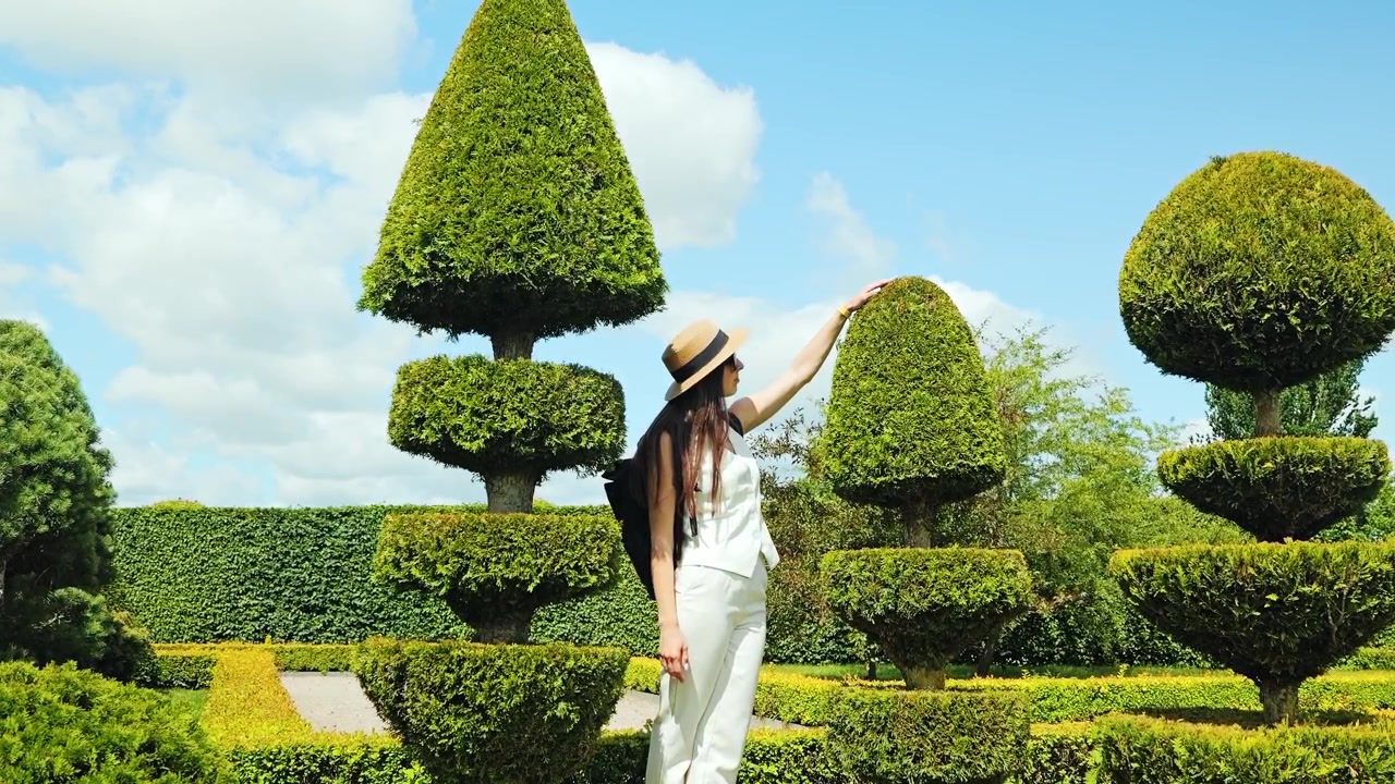 Young woman in white outfit touching topiary in French style garden summer