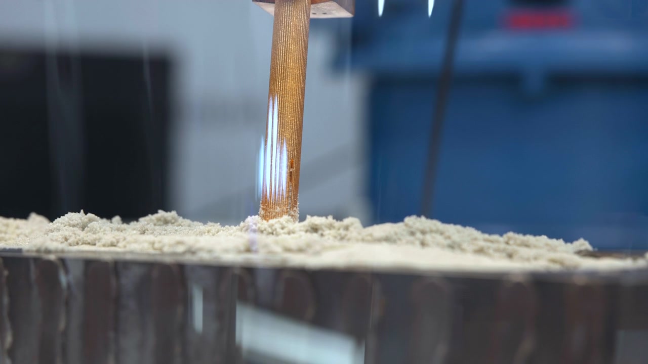 Pala miscelatrice verticale si trova all'interno di un contenitore metallico riempito con pastella chiara e friabile, con attrezzatura blu sfocata sullo sfondo, illuminazione morbida e fredda, profondità di campo ridotta, inquadratura ravvicinata centrata.