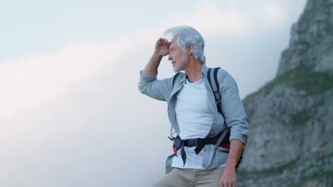 senior man shielding his eyes while standing on a rock 4k