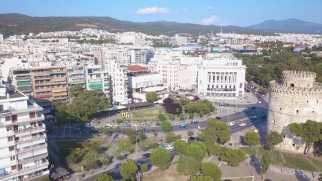 The-White-Tower-Of-Thessaloniki-Opposite-The-National-Theatre-Of-Northern-Greece-And-Aristotle's-Theatre-Building-With-Vehicles-On-The-Road---aerial-drone