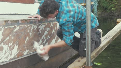 a young carpenter wipes down a sanded boat hull