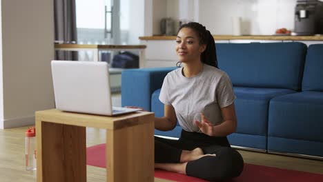 Young-African-woman-doing-yoga-sitting-in-front-the-laptop