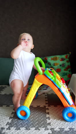 chubby caucasian baby in white bodysuit stands up holding by the walker. kid looks up waving his hand. vertical video.