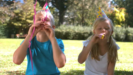 irmãos com chapéu de festa a divertir-se com a buzina da festa.