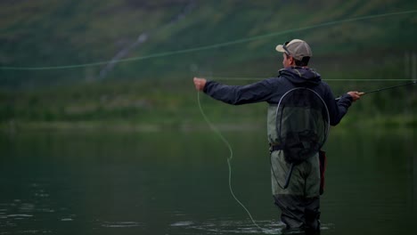 young man casts fly fishing rod back and forth at calm lake, side view