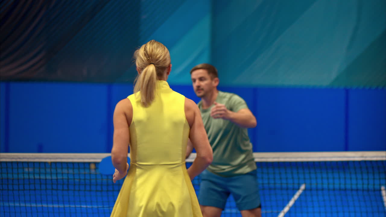 A man and a woman training to play pickleball on a blue, inside court