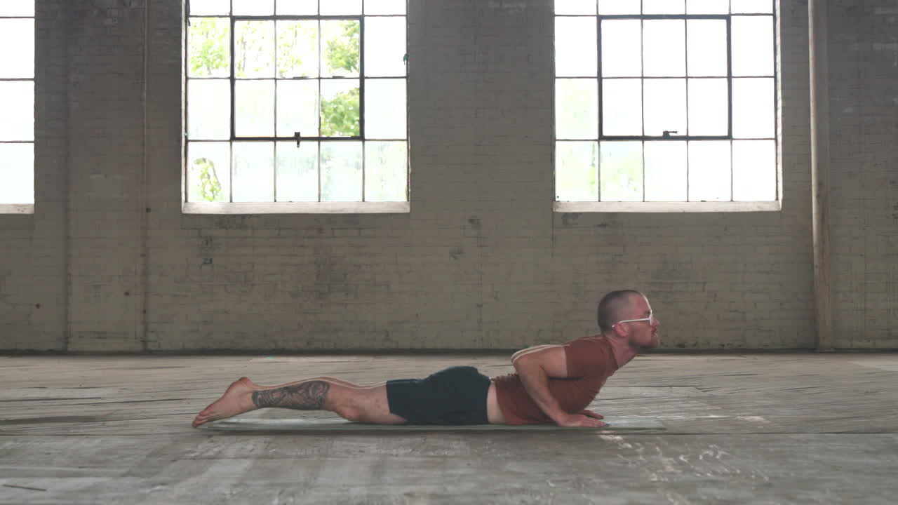Man in an industrial warehouse practicing yoga doing a cobra pose and moving into a plank pose.