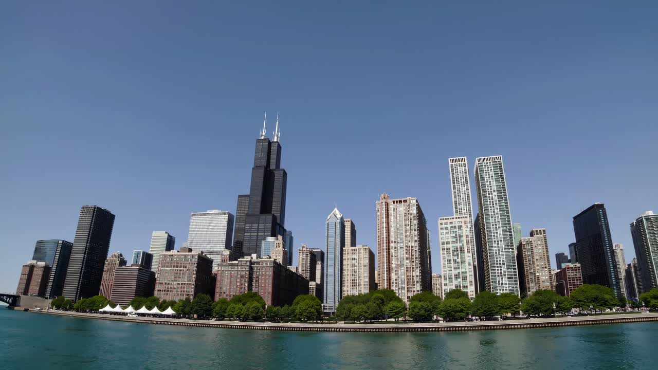 Video grandangolare che riprende una vista dello skyline di moderni grattacieli lungo un lungomare, sotto un cielo sereno.