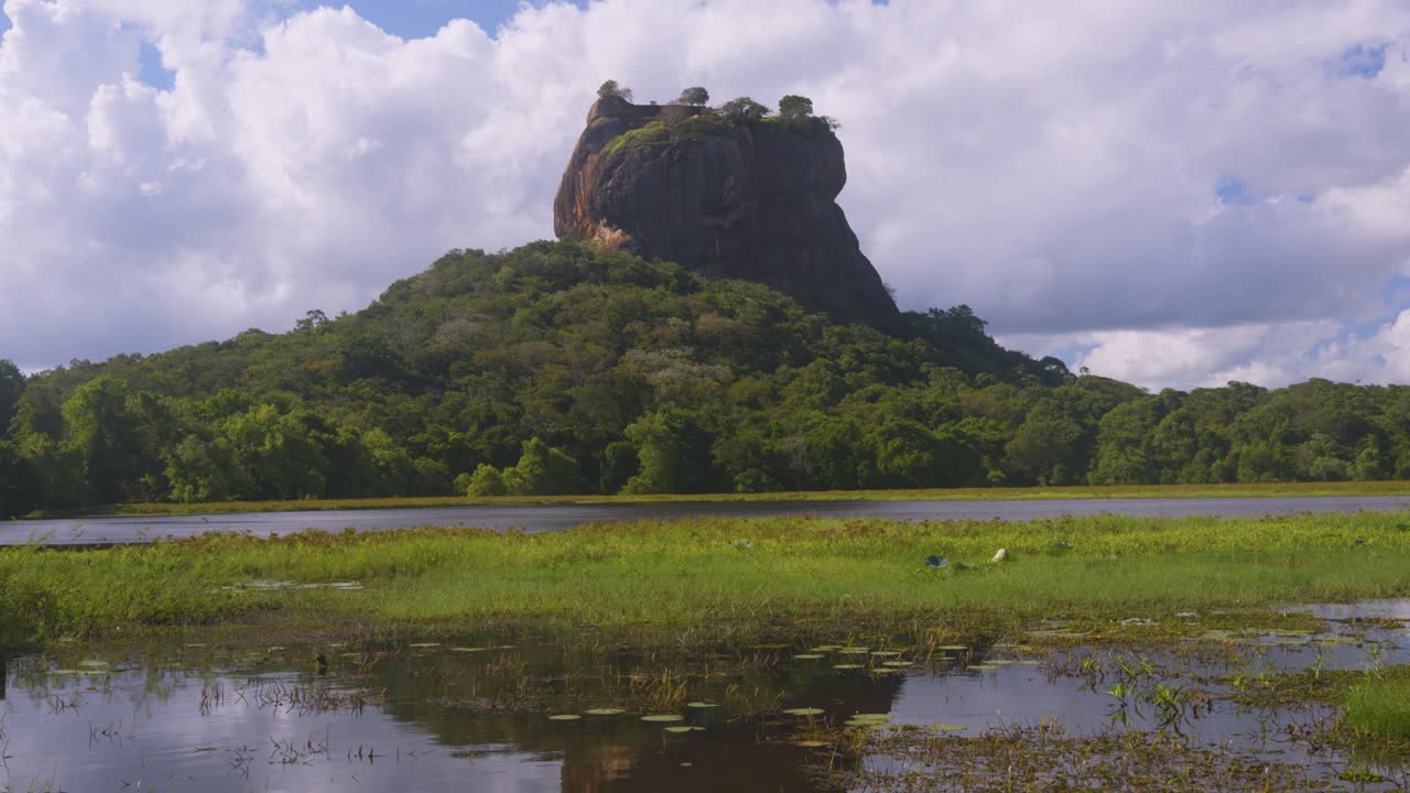 Fortezza rocciosa di Sigiriya sopra pianure verdi, panoramica verticale media che scende fino al calmo e pacifico riflesso nello stagno, Sri Lanka