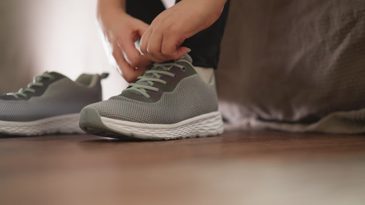 Woman adjusts sneaker tongue at home closeup. Sportswoman with shoes prepares for running in domestic gym slow motion. Active lifestyle
