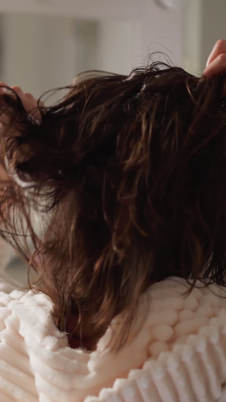 mujer morena sacude el cabello mojado con las manos mirando en el espejo en cámara lenta. dama endereza el cabello oscuro después de la ducha en el baño acogedor con lámparas