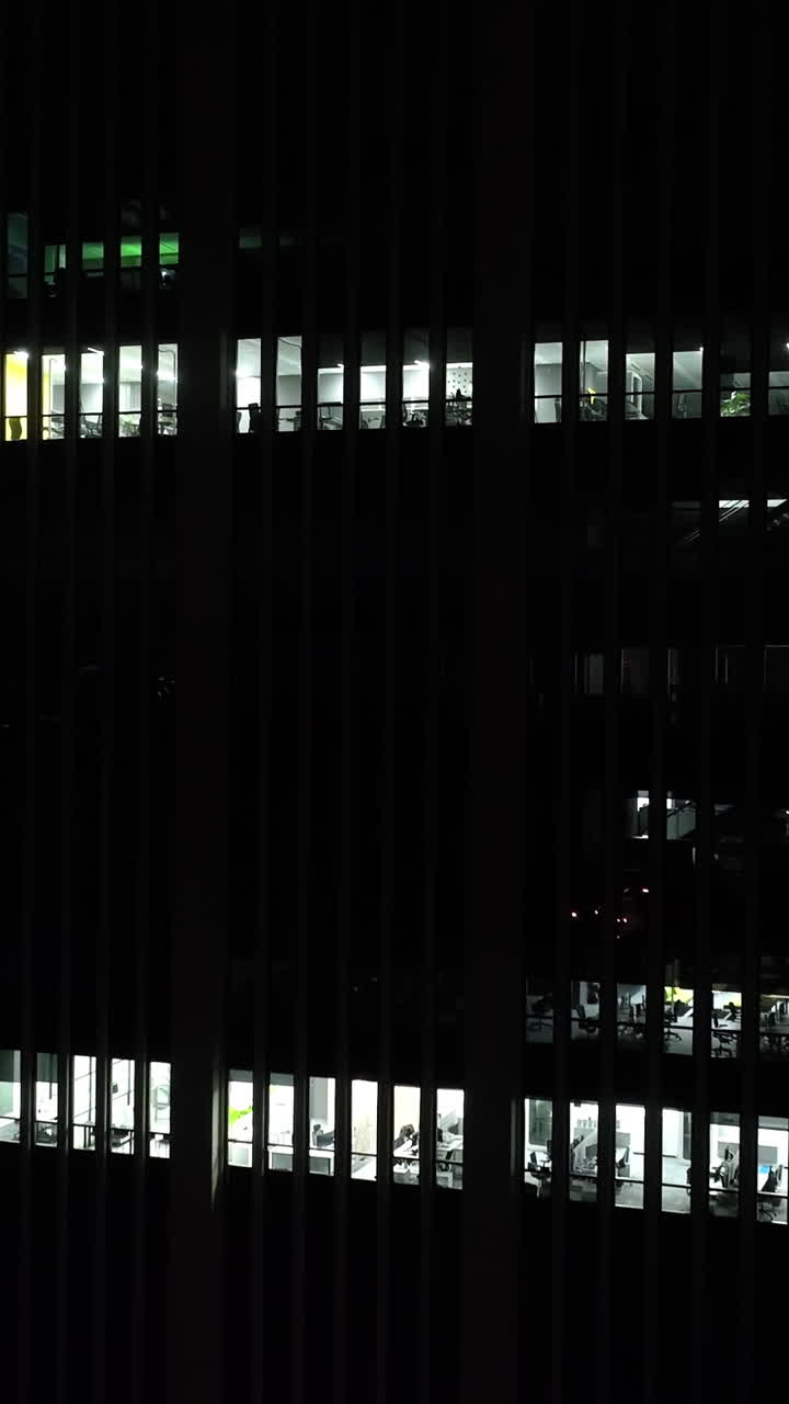 Vertical drone shot around office windows on a corporate building, night darkness