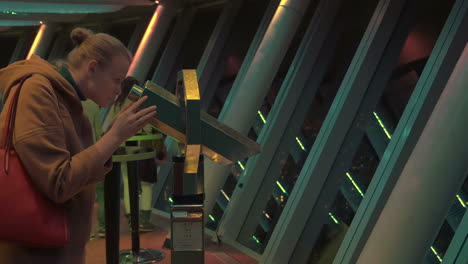 mujer usando el telescopio para disfrutar de la vista nocturna de la ciudad